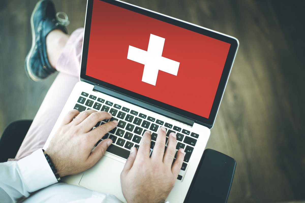 Image of man typing on laptop keyboard with Swiss flag on the screen